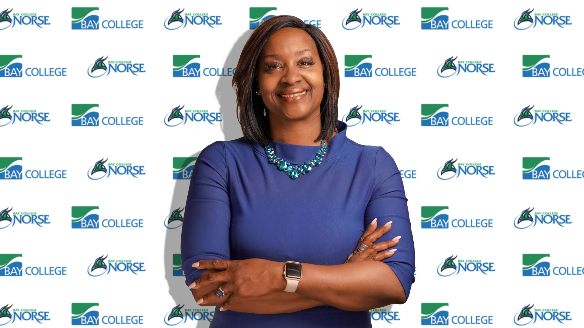 President of Bay De Noc Community College Dr. Nerita Hughes standing in front of a backdrop of Bay college and Bay College Norse logos.