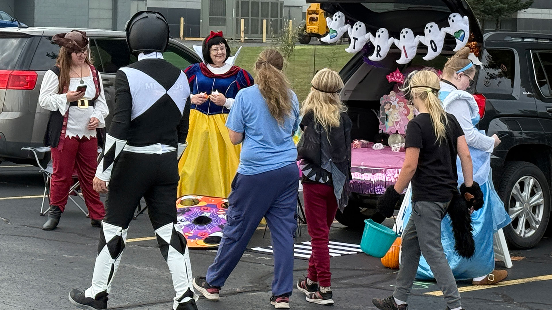 A group of children at the back of a station wagon decorated by TRIO Student Support Services are greeted by employees dressed as Disney princesses and a pirate.