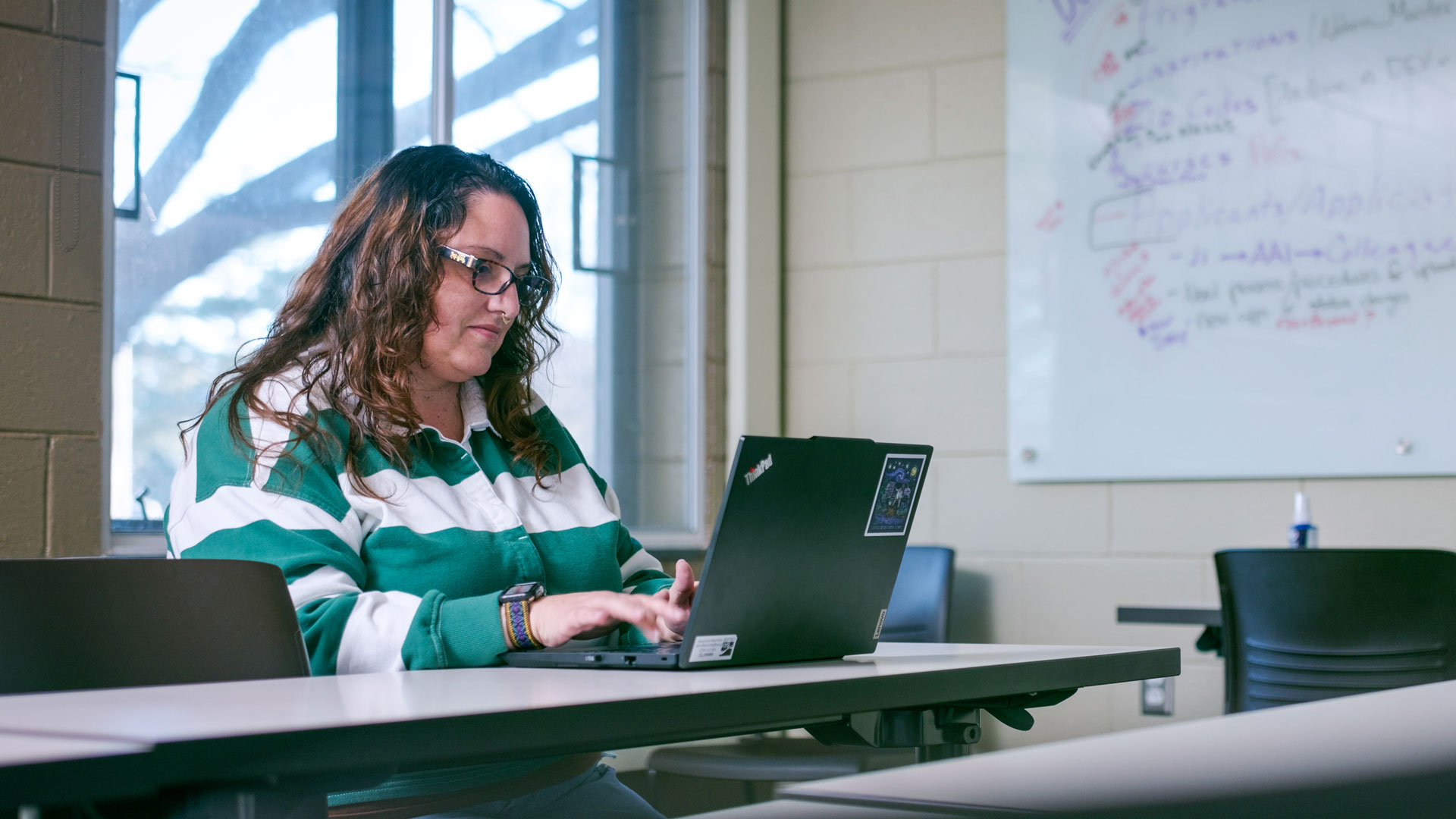Bay College student Christy Koester works on a laptop with her back to the window in a sunlit room.