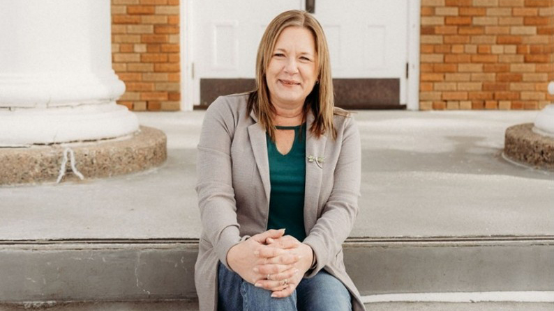 Smiling Bay Alumnus Maggie Shepeard sitting on concrete steps with white pillars in the background to either side.