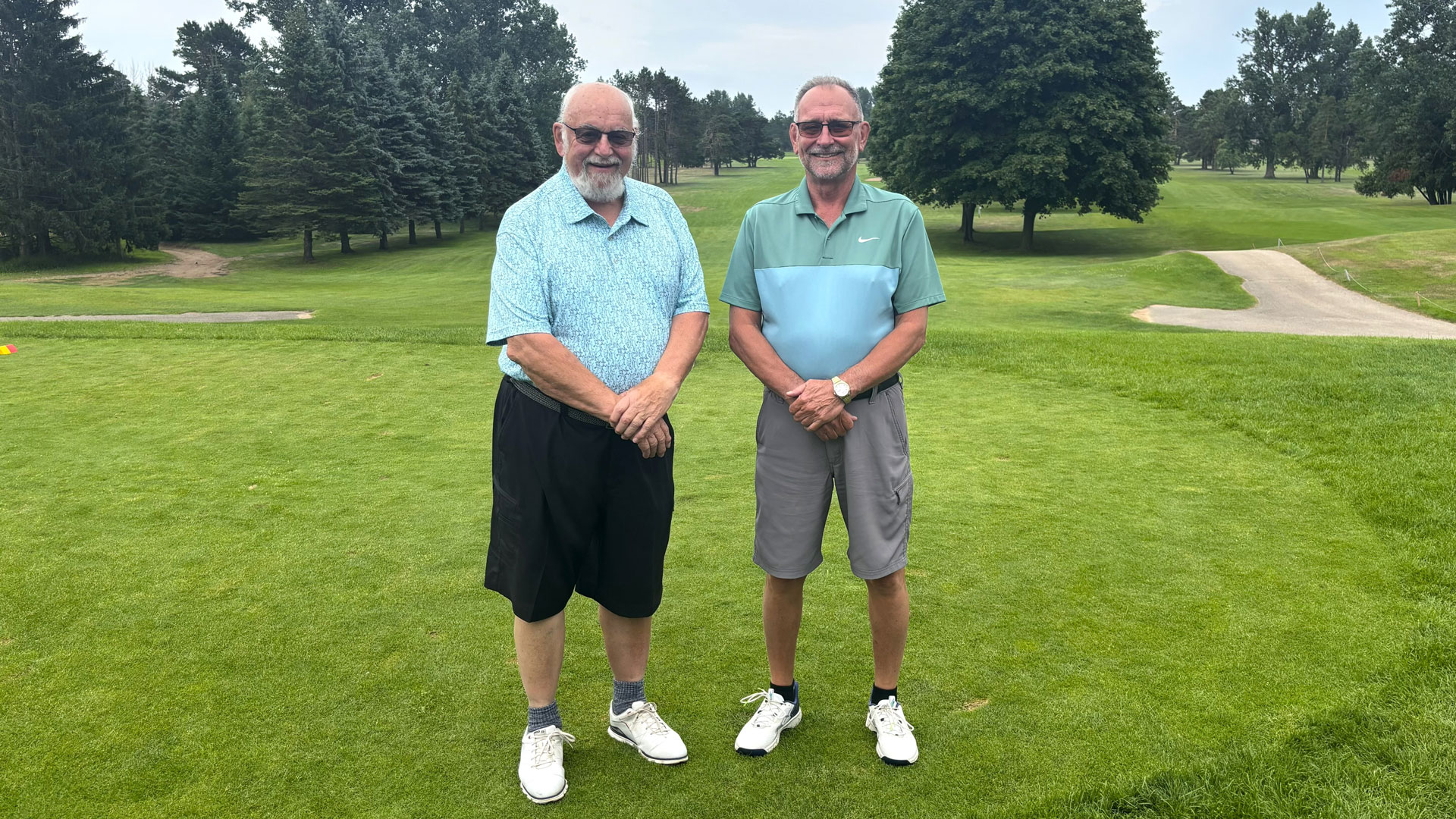 Dave Pechawer smiles beside Bill Marmalick on the green, wearing sunglasses and golf shirts and shorts at the Escanaba Golf Course.